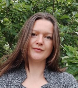 A photo of Sarah Nicmanis standing in front of a leafy background